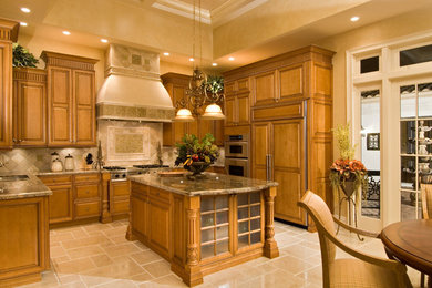 Inredning av ett klassiskt stort kök, med en dubbel diskho, luckor med upphöjd panel, skåp i mellenmörkt trä, granitbänkskiva, beige stänkskydd, stänkskydd i stenkakel, rostfria vitvaror, travertin golv, en köksö och beiget golv