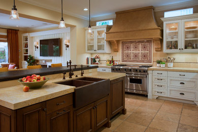 Inspiration for a large mediterranean l-shaped limestone floor and beige floor open concept kitchen remodel in Orange County with a farmhouse sink, recessed-panel cabinets, white cabinets, beige backsplash, stainless steel appliances, limestone backsplash, limestone countertops and an island