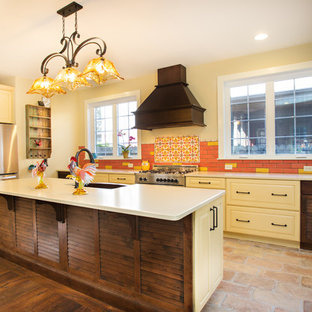 Photo of a mid-sized mediterranean l-shaped eat-in kitchen in DC Metro with a farmhouse sink, raised-panel cabinets, yellow cabinets, multi-coloured splashback, stainless steel appliances, with island, ceramic splashback, brick floors, brown floor, quartz benchtops and white benchtop.