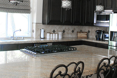 Example of a mid-sized tuscan l-shaped kitchen design in Los Angeles with a double-bowl sink, raised-panel cabinets, dark wood cabinets, granite countertops, beige backsplash, ceramic backsplash, stainless steel appliances, an island and beige countertops