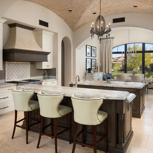 This is an example of an expansive mediterranean u-shaped open plan kitchen in Phoenix with a farmhouse sink, raised-panel cabinets, brown cabinets, quartzite benchtops, multi-coloured splashback, porcelain splashback, stainless steel appliances, porcelain floors, multiple islands, beige floor and multi-coloured benchtop.