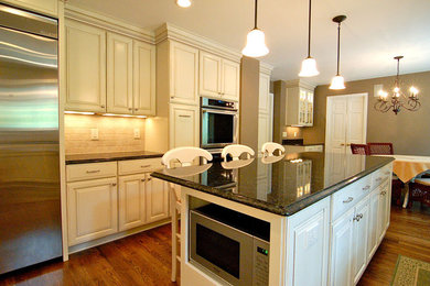 Example of a large tuscan u-shaped medium tone wood floor eat-in kitchen design in DC Metro with an undermount sink, raised-panel cabinets, beige cabinets, granite countertops, beige backsplash, terra-cotta backsplash, stainless steel appliances and an island