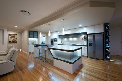 Inredning av ett modernt kök, med en undermonterad diskho, släta luckor, vita skåp, bänkskiva i kvarts, stänkskydd med metallisk yta, glaspanel som stänkskydd, ljust trägolv och en köksö