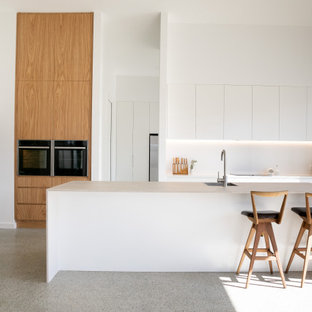 Inspiration for a large contemporary kitchen in Newcastle - Maitland with flat-panel cabinets, white cabinets, quartz benchtops, white splashback, concrete floors, with island, a single-bowl sink, stainless steel appliances, grey floor and white benchtop.