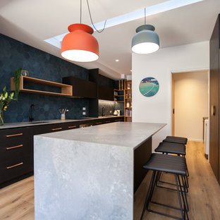Mid-sized contemporary u-shaped eat-in kitchen in Hobart with black cabinets, solid surface benchtops, blue splashback, stainless steel appliances, light hardwood floors, with island and an undermount sink.