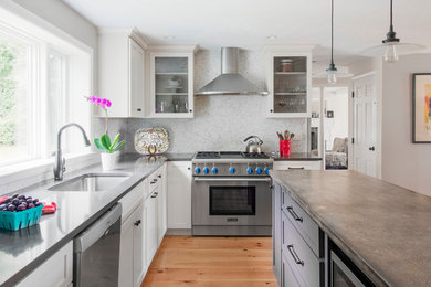 Example of a transitional l-shaped medium tone wood floor and brown floor kitchen design in Boston with an undermount sink, shaker cabinets, white cabinets, gray backsplash, mosaic tile backsplash, stainless steel appliances, an island and gray countertops