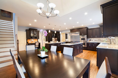 Large transitional l-shaped light wood floor eat-in kitchen photo in New York with shaker cabinets, dark wood cabinets, granite countertops, gray backsplash, matchstick tile backsplash, stainless steel appliances, an undermount sink and two islands