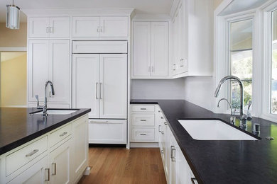 Example of a transitional l-shaped medium tone wood floor eat-in kitchen design in San Francisco with recessed-panel cabinets, white cabinets, granite countertops, white backsplash, ceramic backsplash, an island, an undermount sink and paneled appliances