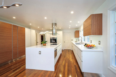 Example of a large trendy medium tone wood floor kitchen design in San Francisco with a drop-in sink, flat-panel cabinets, white cabinets, quartz countertops, white backsplash, stainless steel appliances and an island