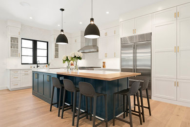 Mid-sized farmhouse l-shaped light wood floor and brown floor kitchen photo in San Francisco with a farmhouse sink, shaker cabinets, white cabinets, white backsplash, stainless steel appliances, an island and white countertops
