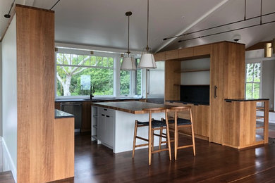 Mid-sized trendy u-shaped dark wood floor and brown floor open concept kitchen photo in Boston with an undermount sink, flat-panel cabinets, dark wood cabinets, wood countertops, black backsplash, stone slab backsplash, stainless steel appliances, an island and brown countertops