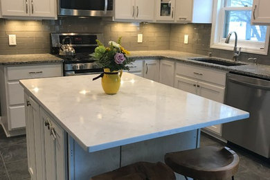 Example of a mid-sized transitional u-shaped porcelain tile and black floor kitchen design in Milwaukee with an undermount sink, recessed-panel cabinets, white cabinets, granite countertops, gray backsplash, glass tile backsplash and stainless steel appliances