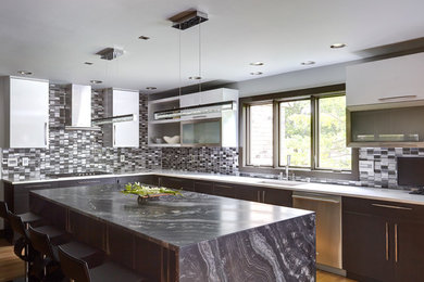 Huge trendy u-shaped light wood floor open concept kitchen photo in Milwaukee with an undermount sink, flat-panel cabinets, white cabinets, quartz countertops, black backsplash, glass tile backsplash, stainless steel appliances and an island