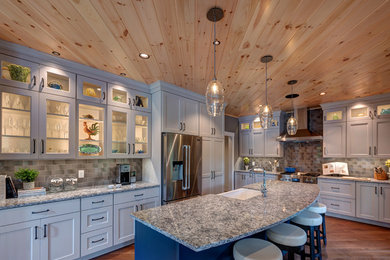 Example of a large transitional l-shaped medium tone wood floor kitchen design in Boston with a farmhouse sink, glass-front cabinets, white cabinets, granite countertops, gray backsplash, subway tile backsplash, stainless steel appliances and an island