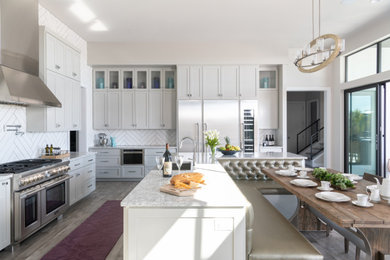 Transitional u-shaped medium tone wood floor and brown floor eat-in kitchen photo in Austin with a farmhouse sink, shaker cabinets, gray cabinets, white backsplash, stainless steel appliances, an island and gray countertops