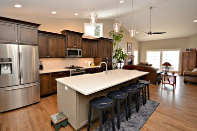 Example of a large classic single-wall medium tone wood floor and brown floor open concept kitchen design in Boise with a farmhouse sink, recessed-panel cabinets, dark wood cabinets, quartz countertops, white backsplash, subway tile backsplash, stainless steel appliances and an island