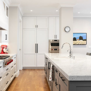 Transitional l-shaped medium tone wood floor and brown floor kitchen photo in Salt Lake City with an undermount sink, shaker cabinets, white cabinets, white backsplash, stainless steel appliances, an island and white countertops