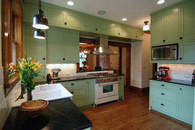 Inspiration for a mid-sized timeless medium tone wood floor kitchen remodel in Minneapolis with a farmhouse sink, shaker cabinets, green cabinets, soapstone countertops, white backsplash and ceramic backsplash
