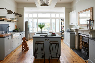 Medium sized classic open plan kitchen in Essex with a belfast sink, shaker cabinets, grey cabinets, black splashback, medium hardwood flooring, an island, brown floors and black worktops.