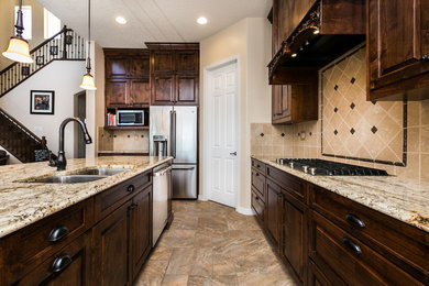 Example of a large classic l-shaped ceramic tile and multicolored floor eat-in kitchen design in Albuquerque with an undermount sink, dark wood cabinets, granite countertops, beige backsplash, stone tile backsplash, stainless steel appliances, an island and raised-panel cabinets