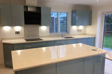 This is an example of a modern kitchen in Hampshire with a submerged sink, flat-panel cabinets, quartz worktops, black appliances and an island.