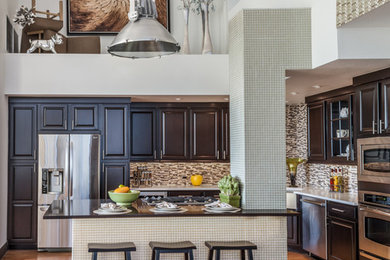 Mid-sized transitional l-shaped light wood floor open concept kitchen photo in Las Vegas with a farmhouse sink, raised-panel cabinets, brown cabinets, quartzite countertops, multicolored backsplash, glass tile backsplash, stainless steel appliances and an island