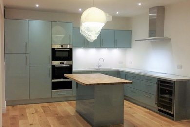 Photo of a medium sized contemporary l-shaped open plan kitchen in Other with an integrated sink, flat-panel cabinets, quartz worktops, stainless steel appliances, medium hardwood flooring, an island and white worktops.