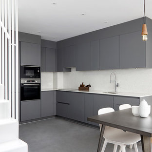 This is an example of a contemporary l-shaped kitchen/diner in London with a submerged sink, flat-panel cabinets, grey cabinets, white splashback, black appliances, no island, grey floors, white worktops and concrete flooring.