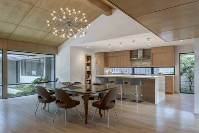 Example of a mid-sized 1950s galley light wood floor eat-in kitchen design in Dallas with an undermount sink, flat-panel cabinets, light wood cabinets, quartz countertops, beige backsplash, glass tile backsplash, stainless steel appliances, an island and white countertops