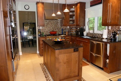 Example of a mid-sized transitional porcelain tile kitchen design in Detroit with an undermount sink, shaker cabinets, brown cabinets, granite countertops, multicolored backsplash, glass tile backsplash, stainless steel appliances and an island