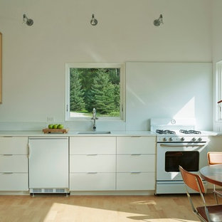 Inspiration for a small contemporary l-shaped eat-in kitchen in Burlington with an undermount sink, flat-panel cabinets, white cabinets, concrete benchtops, white splashback, white appliances, light hardwood floors and no island.