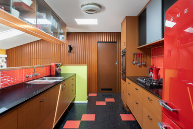 Photo of a medium sized midcentury galley enclosed kitchen in Melbourne with a single-bowl sink, ceramic splashback, black appliances, multi-coloured floors and red splashback.