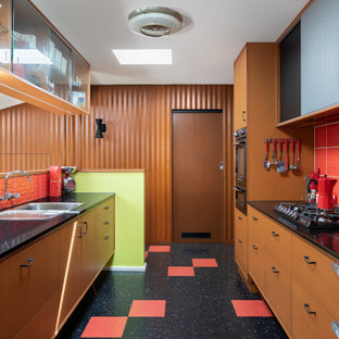 Photo of a mid-sized midcentury galley separate kitchen in Melbourne with a single-bowl sink, ceramic splashback, black appliances, multi-coloured floor and red splashback.