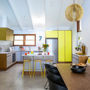 Expansive midcentury l-shaped open plan kitchen in Adelaide with an integrated sink, flat-panel cabinets, grey cabinets, solid surface benchtops, white splashback, porcelain splashback, stainless steel appliances, concrete floors and with island.