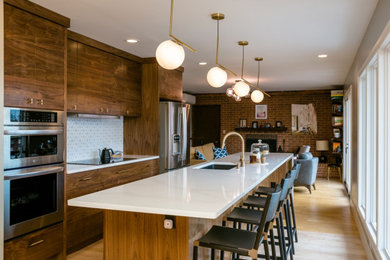 Inspiration for a mid-sized 1950s galley light wood floor and brown floor eat-in kitchen remodel with a single-bowl sink, flat-panel cabinets, dark wood cabinets, quartz countertops, white backsplash, ceramic backsplash, stainless steel appliances, an island and white countertops