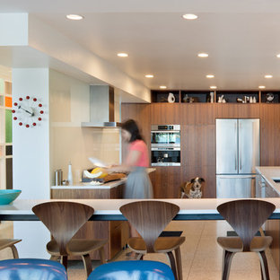 Foto de cocina comedor en U y barra de cocina, moderna, con armarios con paneles lisos, salpicadero de vidrio templado, electrodomésticos de acero inoxidable, puertas de armario de madera en tonos medios, fregadero bajoencimera, encimera de granito, salpicadero blanco, península, suelo de corcho y suelo beige