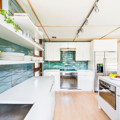 Inspiration for a mid-sized mid-century modern u-shaped light wood floor kitchen remodel in Los Angeles with a drop-in sink, flat-panel cabinets, white cabinets, quartz countertops, blue backsplash, ceramic backsplash, stainless steel appliances and a peninsula