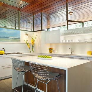 This is an example of a mid-sized midcentury l-shaped kitchen in DC Metro with an undermount sink, flat-panel cabinets, white cabinets, laminate benchtops, white splashback, with island and brown floor.