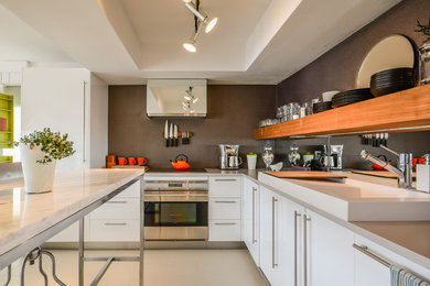 Example of a trendy l-shaped kitchen design in Orlando with an integrated sink, flat-panel cabinets, white cabinets, stainless steel appliances and an island