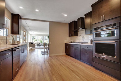 Open concept kitchen - large 1950s galley light wood floor and beige floor open concept kitchen idea in Portland with an undermount sink, flat-panel cabinets, dark wood cabinets, quartzite countertops, white backsplash, porcelain backsplash, stainless steel appliances, no island and white countertops