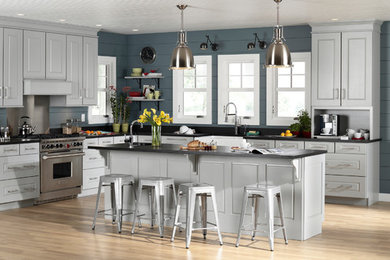 Inspiration for a medium sized traditional l-shaped kitchen/diner in Orlando with a belfast sink, raised-panel cabinets, white cabinets, soapstone worktops, blue splashback, wood splashback, stainless steel appliances, light hardwood flooring, an island, beige floors and black worktops.