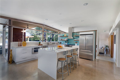 Mid-sized 1960s l-shaped concrete floor open concept kitchen photo in Phoenix with an undermount sink, flat-panel cabinets, white cabinets, quartz countertops, blue backsplash, glass tile backsplash, stainless steel appliances and an island