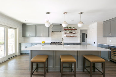 Mid-sized transitional l-shaped medium tone wood floor and brown floor kitchen photo in Charleston with a farmhouse sink, shaker cabinets, gray cabinets, beige backsplash, subway tile backsplash, stainless steel appliances, an island and white countertops