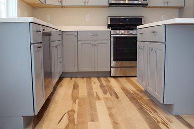 Moderne Wohnküche in L-Form mit Unterbauwaschbecken, Schrankfronten im Shaker-Stil, grauen Schränken, Mineralwerkstoff-Arbeitsplatte, Küchenrückwand in Weiß, Küchengeräten aus Edelstahl, hellem Holzboden und Kücheninsel in Burlington