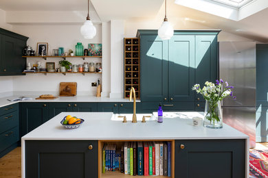 ロンドンにある高級な中くらいなトランジショナルスタイルのおしゃれなキッチン (ドロップインシンク、シェーカースタイル扉のキャビネット、緑のキャビネット、御影石カウンター、白いキッチンパネル、セラミックタイルのキッチンパネル、黒い調理設備、淡色無垢フローリング、茶色い床、白いキッチンカウンター) の写真