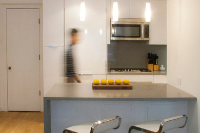 ニューヨークにある小さなモダンスタイルのおしゃれなキッチン (フラットパネル扉のキャビネット、白いキャビネット、人工大理石カウンター、グレーのキッチンパネル、シルバーの調理設備) の写真