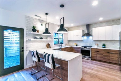 Large contemporary u-shaped kitchen in Atlanta with a submerged sink, flat-panel cabinets, white cabinets, composite countertops, white splashback, ceramic splashback, stainless steel appliances, medium hardwood flooring, a breakfast bar, brown floors and white worktops.