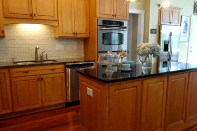 Example of a mid-sized trendy l-shaped dark wood floor eat-in kitchen design in Manchester with a double-bowl sink, raised-panel cabinets, light wood cabinets, granite countertops, white backsplash, ceramic backsplash, stainless steel appliances and an island