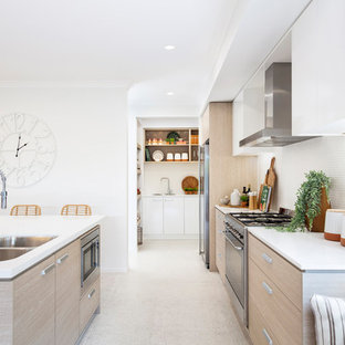 Photo of a beach style galley eat-in kitchen in Brisbane with a double-bowl sink, flat-panel cabinets, medium wood cabinets, white splashback, mosaic tile splashback, stainless steel appliances, with island, beige floor and white benchtop.