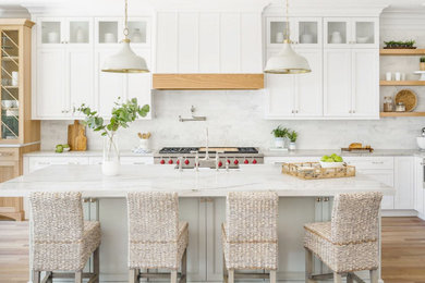 Large beach style l-shaped light wood floor and beige floor eat-in kitchen photo in Charlotte with a farmhouse sink, shaker cabinets, white cabinets, quartzite countertops, gray backsplash, marble backsplash, stainless steel appliances, an island and white countertops